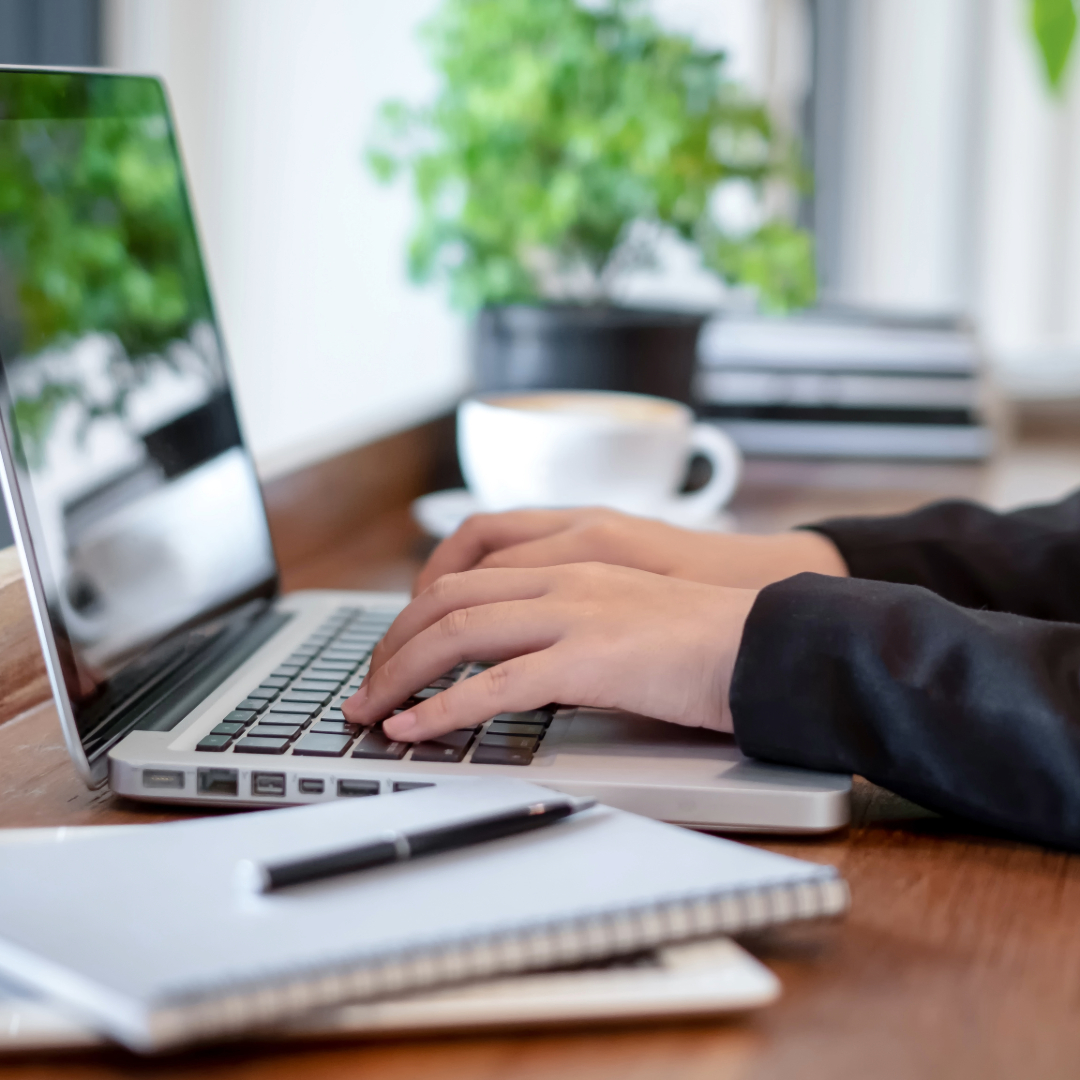 Mãos digitando em um notebook sobre uma mesa de trabalho